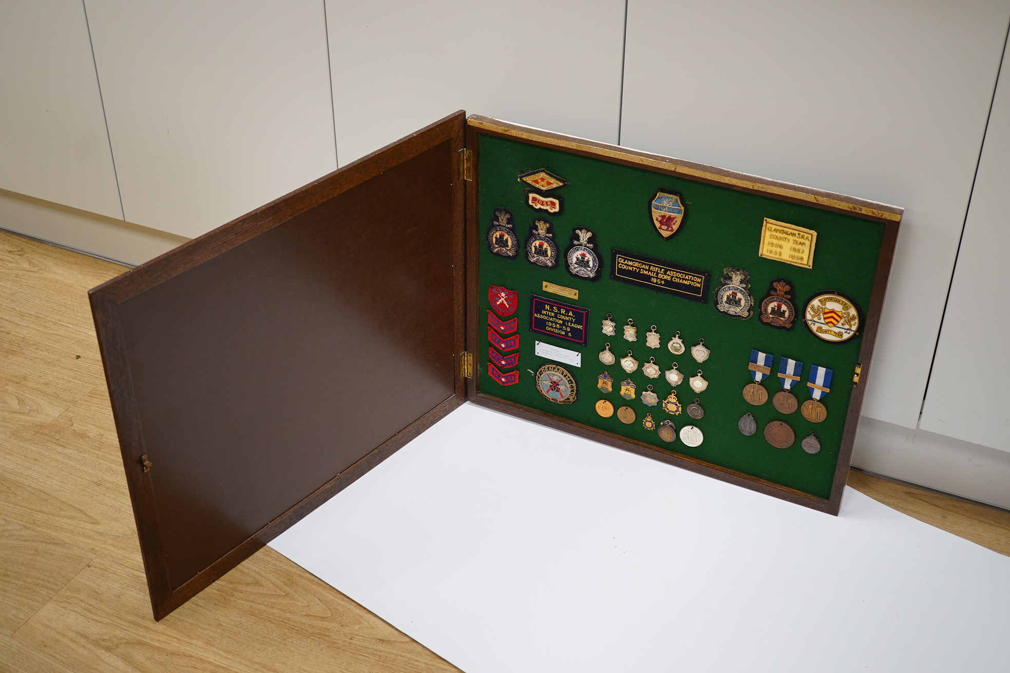 An oak cased collection of rifle and shooting medals disguised as a framed map of Glamorganshire, containing hallmarked silver medals engraved to the awardees, cloth badges for Glamorgan Rifle Association, bronze rifle a